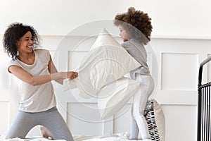 African mother holding pillow fighting with little daughter