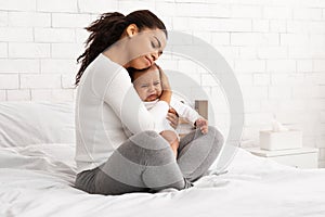 African Mother Hushing Crying Newborn Baby To Sleep In Bedroom