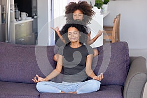 African mother and little daughter meditating on couch at home