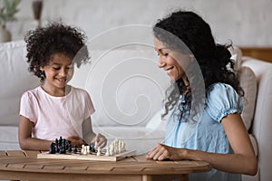 African mother and little daughter play chess game at home