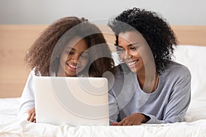 African mother lying on bed with teen daughter browsing internet