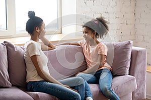 African mother and pre-teen daughter talking seated on couch