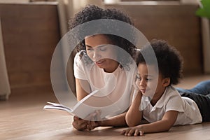 African mother reading fairy tale to son lying on floor