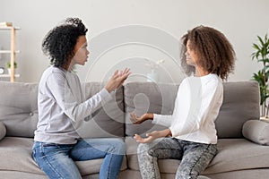 African mother scolding teen daughter sitting on couch at home