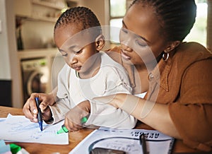 African mother and small child drawing together at a desk at home. Caring, working woman making family time to play with