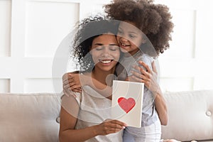 African mum hugging daughter holding greeting card on mothers day