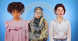 African, Muslim and European open their eyes and look sternly at the camera isolated against a blue background