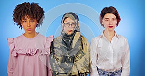 African, Muslim and European open their eyes and look sternly at the camera isolated against a blue background