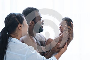 African Nigerian father and Asian mother carrying holding cute newborn baby in parents hands, smiling looking at infant with love