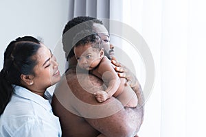 African Nigerian father holding cute newborn baby on shoulder in arms with Asian mother smiling looking at infant with love at