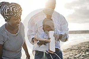 African parents and little son having fun with wood airplane on the beach - Focus on baby hands holding toy