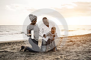 African parents and little son having fun with wood toy airplane on beach at sunset - Focus on faces