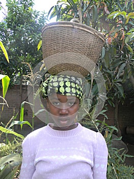 African peasant girl carrying reed basket on head.