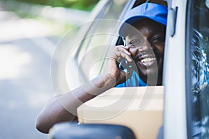 African postal delivery courier man using smart phone and delivering package in car