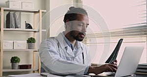 African radiologist examining x-ray film checkup results texting on laptop