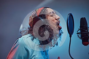 African Rastafarian singer male wearing a blue shirt and beanie emotionally writing song in the recording studio.