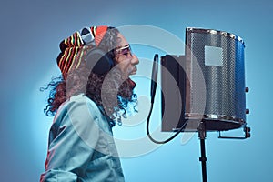 African Rastafarian singer male wearing a blue shirt and beanie emotionally writing song in the recording studio.