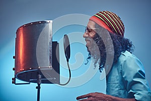 African Rastafarian singer male wearing a blue shirt and beanie emotionally writing song in the recording studio.