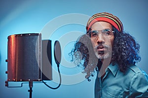 African Rastafarian singer male wearing a blue shirt and beanie emotionally writing song in the recording studio.