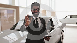 African salesman giving to customer key at new car in showroom.