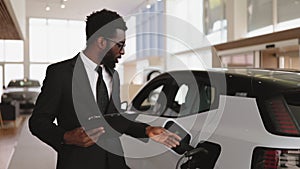 African salesman, selling electric cars in light modern showroom.