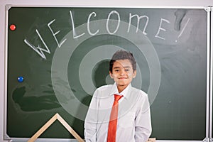 African school boy standing against chalk board with welcome word and looking at camera