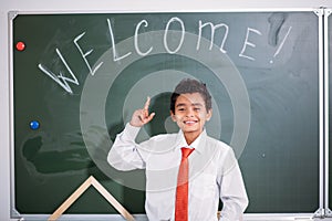 African school boy standing against chalk board with welcome word and looking at camera