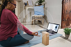 African senior woman doing online yoga lesson at home during lockdown isolation  - Focus on hand