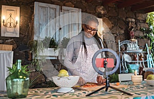 African senior woman streaming online virtual masterclass cooking lesson outdoors at home - Focus on face photo