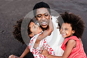 African sisters twins and mother playing on the beach at sunset time during summer vacation - Main focus on girls faces