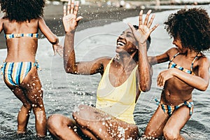 African sisters twins playing on the beach with smiling mother - Black family people having fun on summer time - Main focus on mum