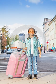 African smiling girl holding pink luggage in city