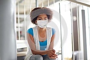 African student girl in mask sitting on stairs