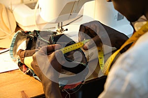 African tailor measuring with a measure tape, near by a sewing machine at sewing workshop