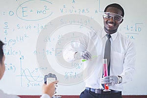 African teacher is doing science experiments inside the classroom with a scientific equations in background