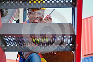 African technician with walky-talkie look through the step of big truck in cargo container shipping area