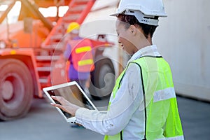 African technician worker woman touch and look to laptop while her co-worker work with construction vehicle