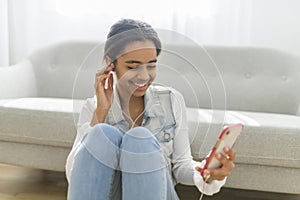 African Teen Girl Sit On Couch At Home using cellphone with earphone