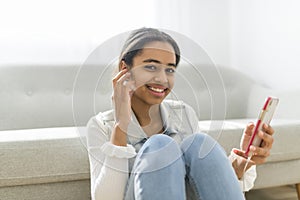 African Teen Girl Sit On Couch At Home using cellphone with earphone