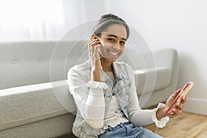 African Teen Girl Sit On Couch At Home using cellphone with earphone