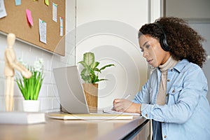 African teen girl student wearing headphones learning with online tutor at home.