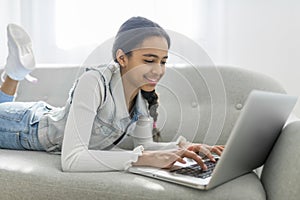 African Teen Girl Using Laptop Computer Browsing Internet Sitting On Couch At Home