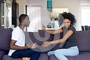 African unhappy married couple sitting on couch quarrelling at home