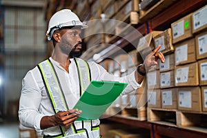 African warehouse manager holding a clipboard checking inventory in a large distribution center