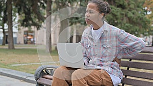 African Woman with Back Pain Using Laptop while Sitting Outdoor on Bench