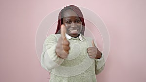 African woman with braided hair smiling with thumbs up over isolated pink background