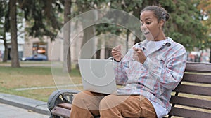 African Woman Celebrating Success on Laptop while Sitting Outdoor on Bench