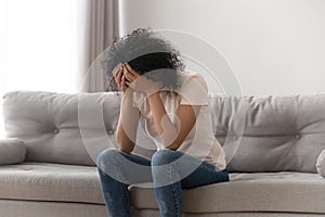 African woman cover face with hands crying sitting on couch