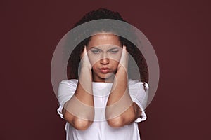 African woman covering ears with her hands, over a green background