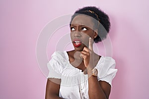 African woman with curly hair standing over pink background thinking worried about a question, concerned and nervous with hand on